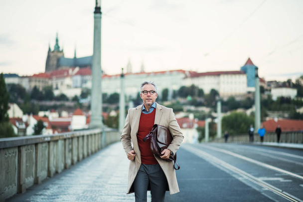 Mature businessman with bag walking on a bridge in Prague city. - Zdjęcie, obraz