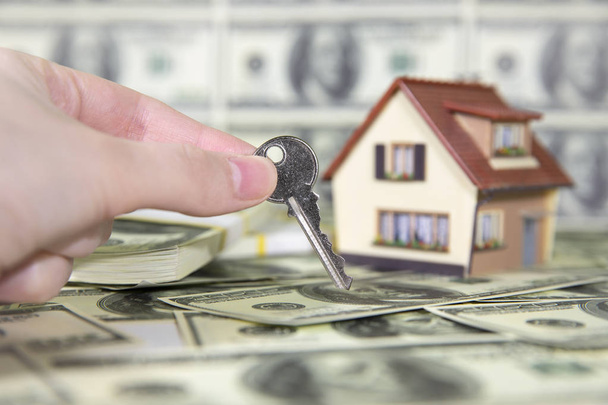 A small house with keys on the background of hundred dollar bills. Reduced copy of the house on the background of money. The keys to the purchased house. - Photo, Image