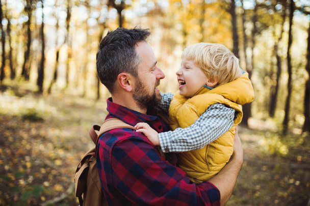 A mature father standing and holding a toddler son in an autumn forest, talking. - Photo, image