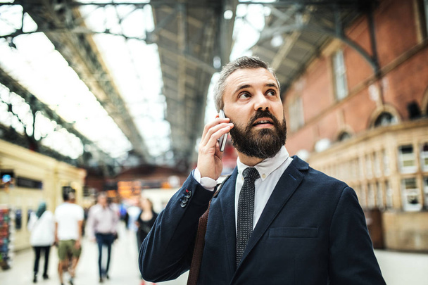 Businessman with smartphone on the trian station in London, making a phone call. - 写真・画像