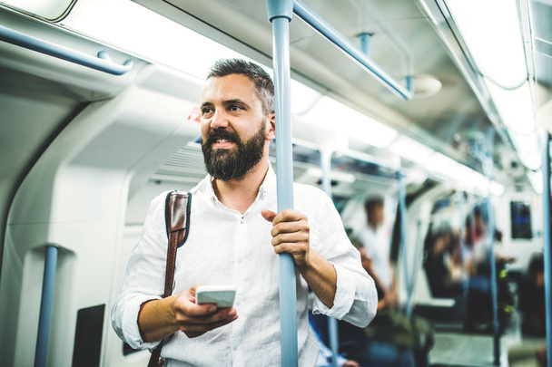 Hipster businessman with smartphone inside the subway in the city, travelling to work. - Photo, Image