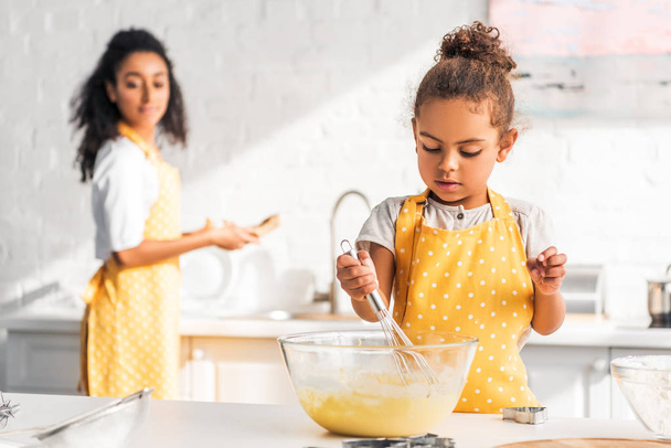 επιλεκτική εστίαση των αφροαμερικάνων κόρη προετοιμασία και χτυπώντας το ζυμάρι στην κουζίνα - Φωτογραφία, εικόνα