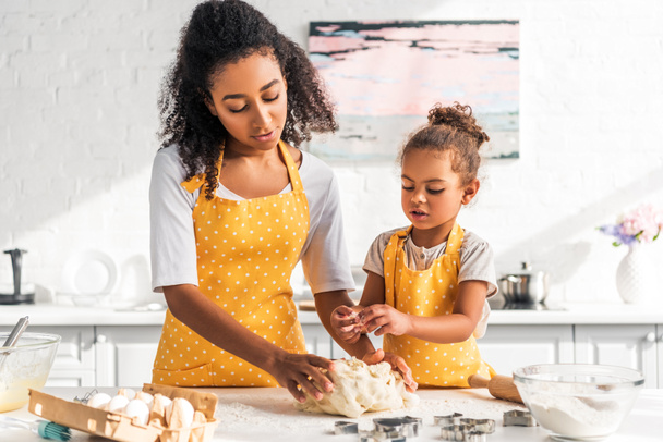 madre e hija afroamericana en delantales amarillos amasando masa en la cocina
 - Foto, Imagen
