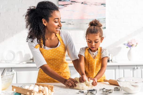attractive african american mother and adorable daughter kneading dough in kitchen - Foto, imagen