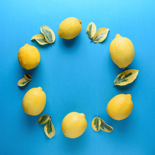 Creative summer pattern made of lemons and green leaves on blue background. Fruit minimal concept. - Фото, зображення
