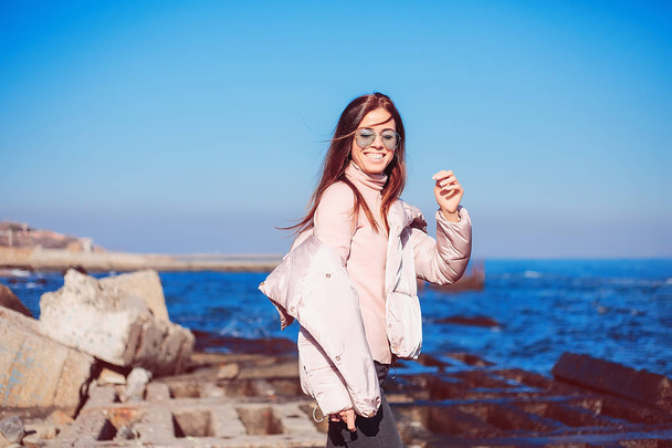 海岸の上を歩くピンクのコートでスタイリッシュな女性  - 写真・画像