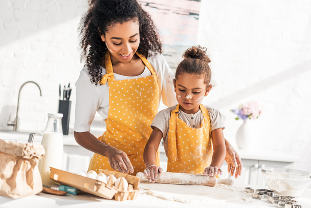 afro-américaine mère aider fille rouler la pâte avec rouleau à pâtisserie dans la cuisine
 - Photo, image