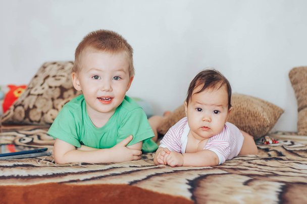 Cute little czterech miesięcy dziewczynka i jej starszy brat, grając pod kołdrą w domu, w łóżku w sypialni, uśmiecha się radośnie - Zdjęcie, obraz