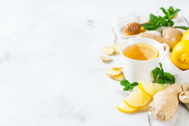 Їжа та напої, концепція охорони здоров'я. Імбирний чайний напій у білій чашці з лимонним м'ятним медом на кухонному столі для холодних та грипу зимових осінніх днів. Копіювати тло простору
 - Фото, зображення