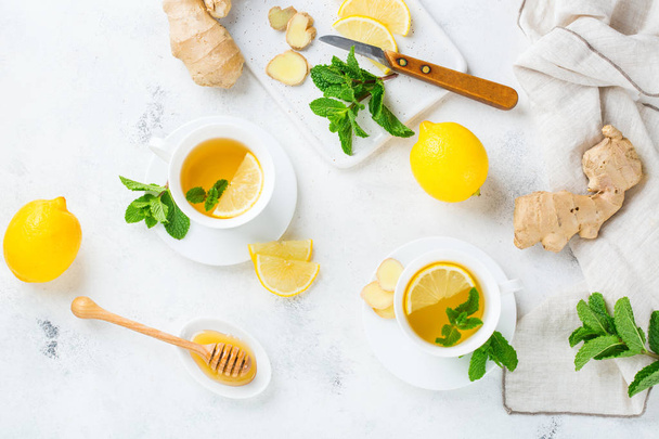 Eten en drinken, stilleven gezondheidszorg concept. Gember thee infusie drank in witte kop met citroen munt honing op een keukentafel voor koude en griep winter herfstdagen. Bovenaanzicht achtergrond - Foto, afbeelding