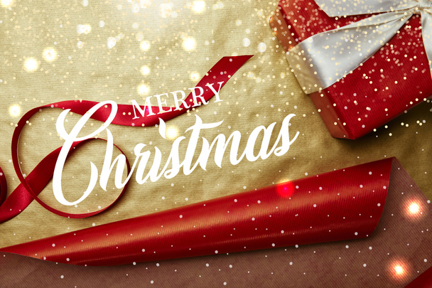top view of gift and ribbon on red and golden wrapping papers background with "merry christmas" lettering - Photo, Image