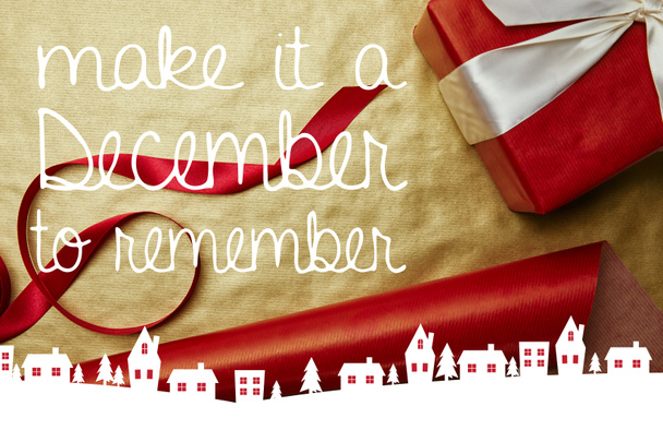 Draufsicht auf Weihnachtsgeschenk und Band auf rotem und goldenem Geschenkpapier Hintergrund mit der Inspiration "Make it a december to remember"  - Foto, Bild