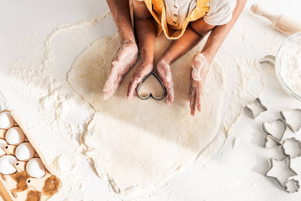 περικομμένη εικόνα των αφροαμερικάνων μητέρα και κόρη προετοιμασία μπισκότα με μούχλα στο τραπέζι στην κουζίνα σε σχήμα καρδιάς - Φωτογραφία, εικόνα