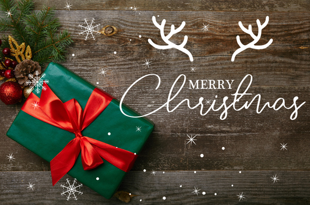 Draufsicht auf verpacktes grünes Geschenk mit roter Schleife und Weihnachtsspielzeug auf Holzgrund mit "Frohe Weihnachten" -Schriftzug - Foto, Bild