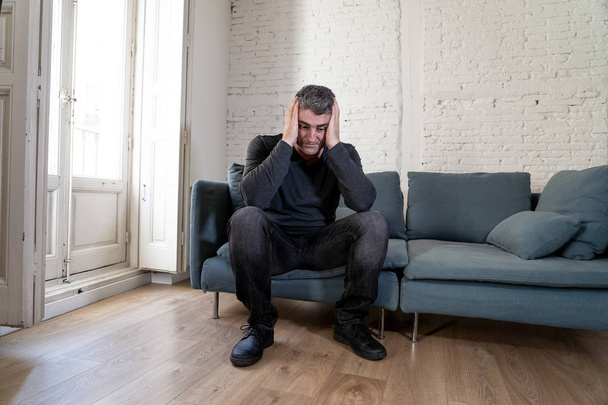 Attractive man feeling desperate sad looking worried depressed thoughtful and lonely suffering depression on couch at home in middle age crisis mental health personal problems and life style concept. - Foto, Bild