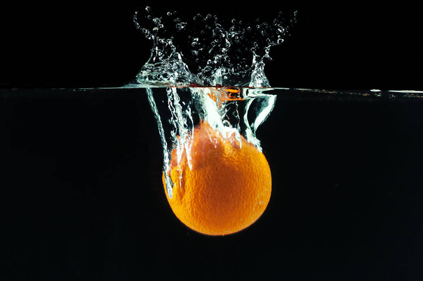 Orange falling into water and making splashes - Фото, изображение