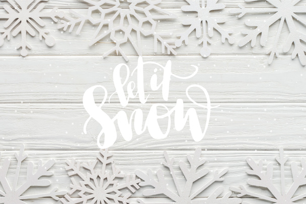 plat lag met decoratieve sneeuwvlokken op witte houten achtergrond met "laat het sneeuw" belettering - Foto, afbeelding