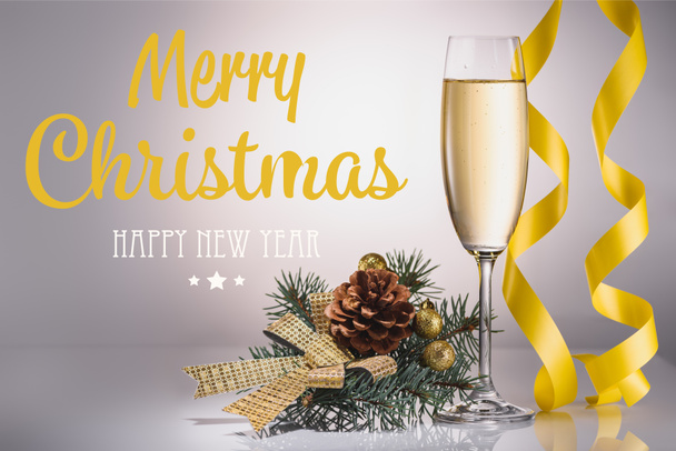 glass of champagne, christmas decoration and confetti on grey backdrop with "merry christmas and happy new year" lettering - Photo, Image