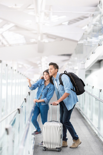 Happy ασιατικό ζευγάρι ταξιδιωτών με αποσκευές στο τερματικό του αεροδρομίου - Φωτογραφία, εικόνα