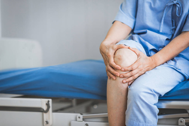 Bliska strzał pacjenta siedzącego na łóżku w szpitalu cierpiącym na ból kolana - Zdjęcie, obraz
