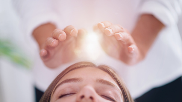 Close up image of relaxed young woman lying with her eyes closed and having Reiki healing treatment in spa center. Energy healing concept.  - Zdjęcie, obraz
