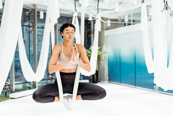 Расслабленная девушка практикует антигравитационную йогу в позе лотоса с жестами мудры намасте в студии
 - Фото, изображение