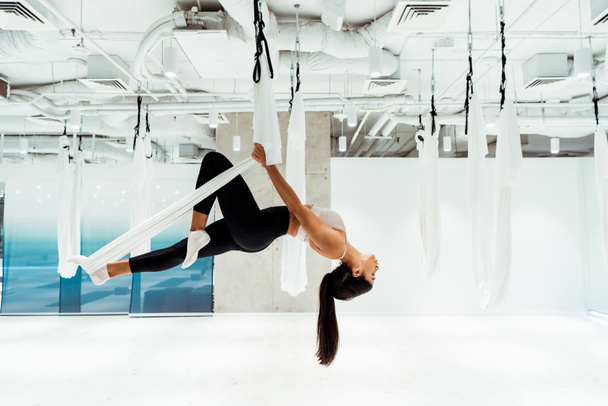 Attractive girl practicing antigravity yoga in inversion position in studio - Fotó, kép