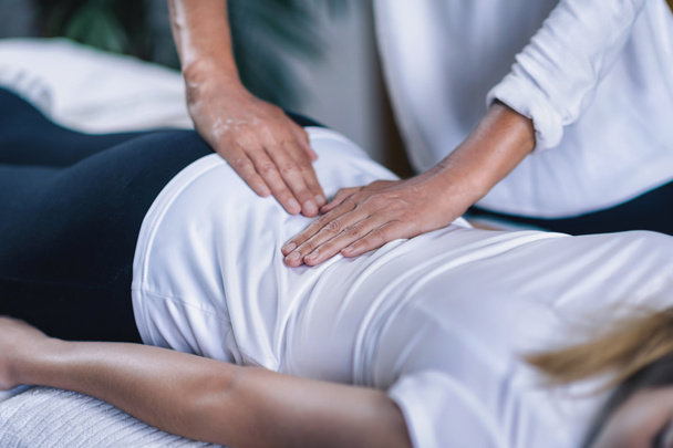 Horizontal image of female Reiki therapist holding hands over teenage patient lower back . Peaceful teenage girl lying. Alternative therapy concept of stress reduction and relaxation.   - Foto, immagini