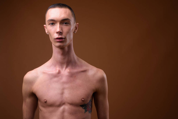 Mladý pohledný muž hermafroditní shirtless proti hnědé poza - Fotografie, Obrázek