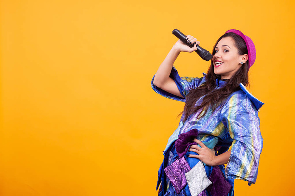Beautiful young woman wearing funky clothes and singing microphone. - Photo, Image