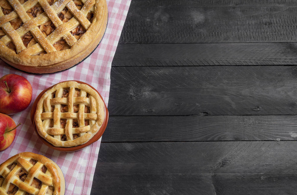 High angle view of differently sized apple pies on a pink kitchen towel, on a black wooden table. Traditional holiday dessert. Holiday home baking. - Photo, Image