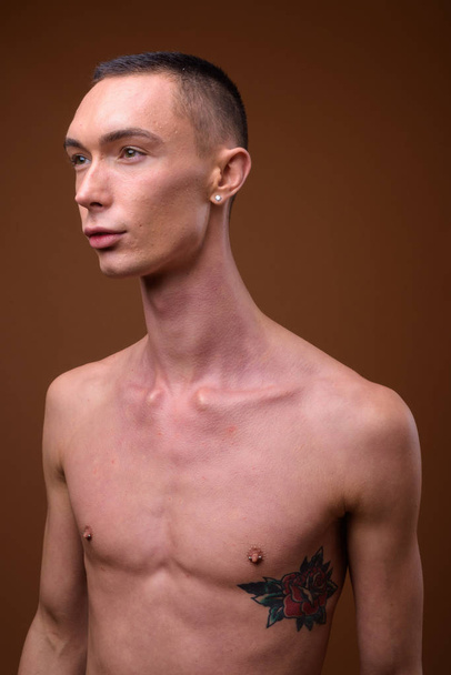 Молодий красивий андрогінний чоловік без сорочки на коричневому фоні
 - Фото, зображення