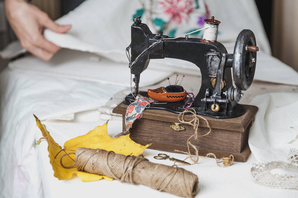 Autumn still life with a sewing machine. Vintage sewing machine and a skein of threads. A yellow maple leaf lies next to it. Behind the canvas with embroider - Φωτογραφία, εικόνα