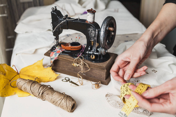 Workplace seamstress. Vintage sewing machine and a skein of threads. A yellow maple leaf lies next to it. The woman's hands fold a flexible tap - Foto, Imagem