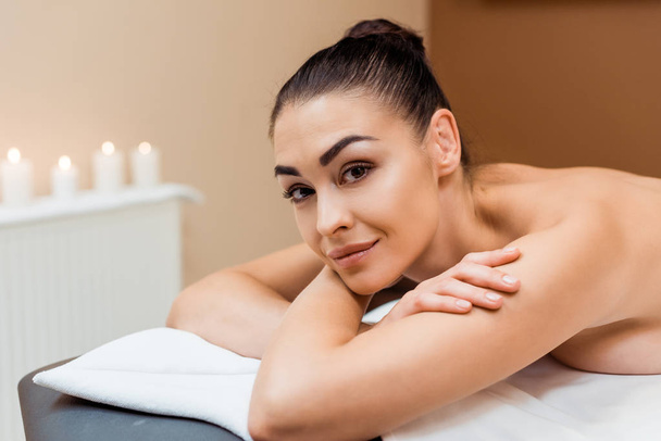 attractive young woman lying on massage table and smiling at camera in spa   - Φωτογραφία, εικόνα