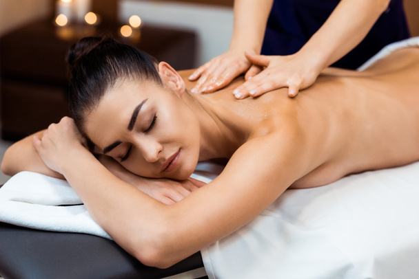 attractive young woman with closed eyes having massage therapy in spa  - Photo, Image