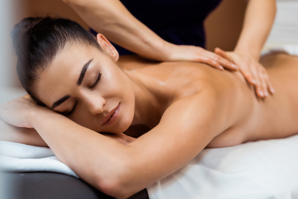 beautiful young woman with closed eyes having massage in spa  - Photo, Image