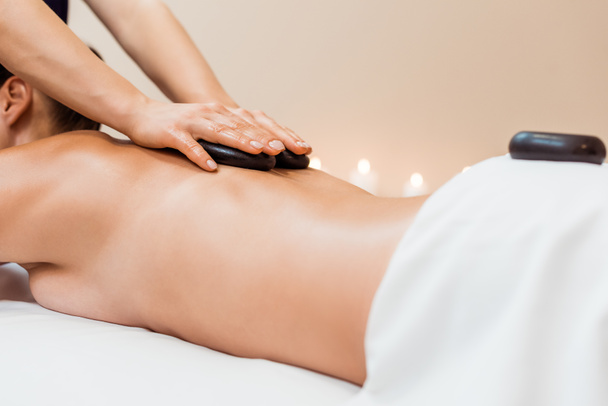 abgeschnittene Aufnahme einer jungen Frau mit Hot-Stone-Massage im Wellness-Salon - Foto, Bild