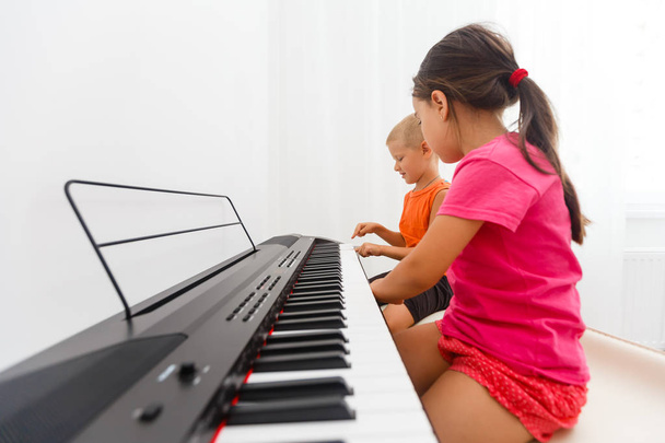 Young girl and boy playing on keyboard  - 写真・画像