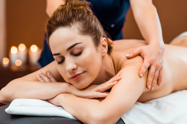 beautiful smiling young woman with closed eyes having massage in spa salon - Zdjęcie, obraz