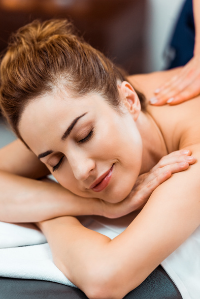 happy young woman with closed eyes enjoying massage in spa salon - 写真・画像