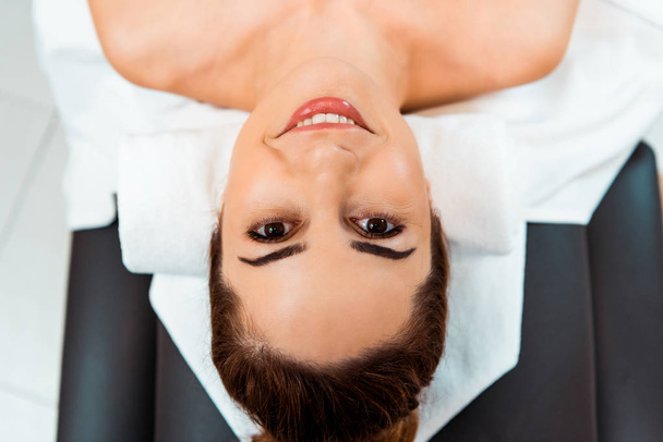 vista superior de la hermosa mujer joven acostada en la mesa de masaje y sonriendo a la cámara
 - Foto, Imagen