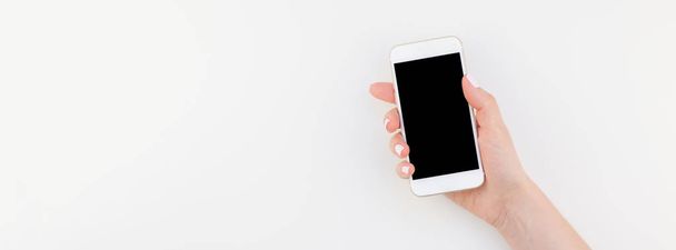 Woman hand with pastel manicure polish holding smartphone isolated on white background with copy space in minimalism style. Long wide banner mock up for feminine blog social technological media - Fotó, kép