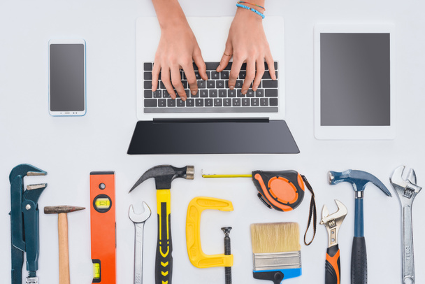 cropped shot of woman using laptop with various tools lying on white - Photo, Image