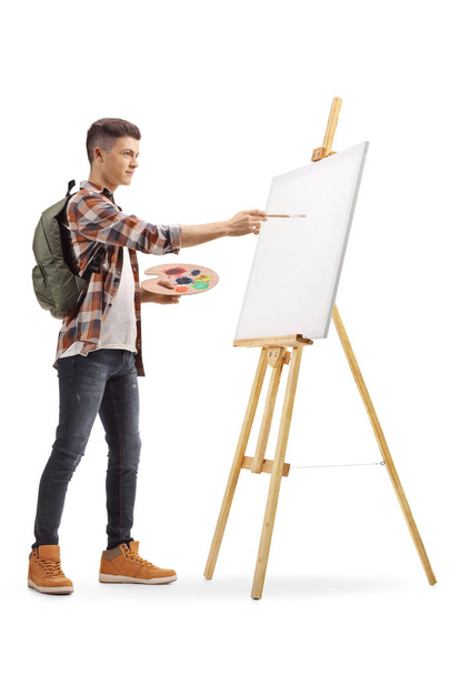 Full length profile shot of a teenage boy painting on a canvas isolated on white background - Fotografie, Obrázek