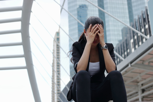 Depressief benadrukt jonge Aziatische zakenvrouw met handen op gezicht zitten in de open lucht. - Foto, afbeelding