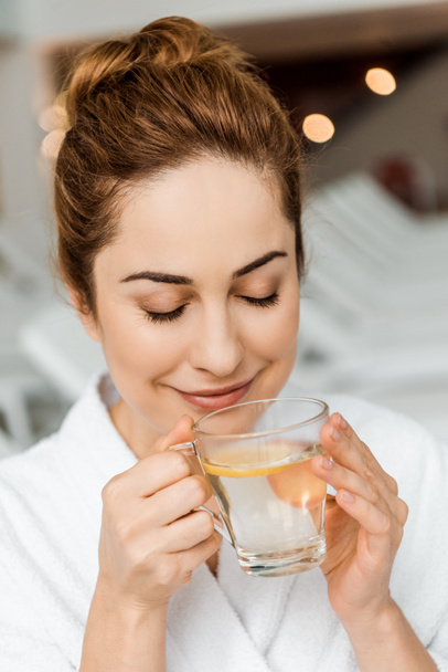 happy young woman holding cup with herbal drink and lemon in spa - Фото, зображення