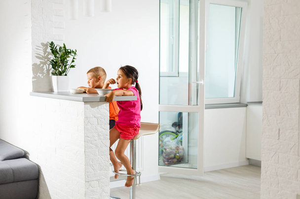 Little brother and sister eating breakfast in white kitchen  - Photo, Image