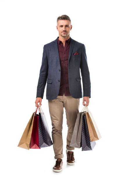 stylish adult man in jacket holding colorful shopping bags isolated on white - Photo, Image