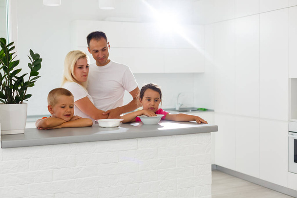 Gelukkige familie eten ontbijt in moderne witte keuken - Foto, afbeelding